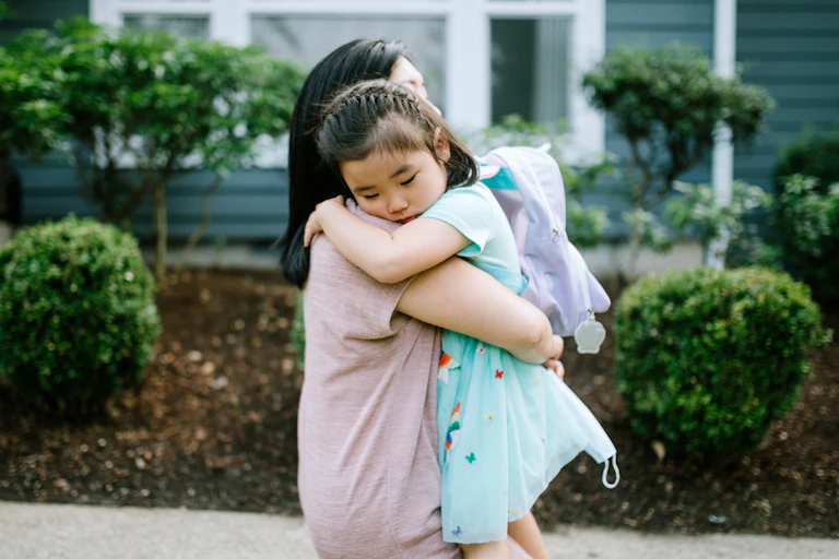 An Asian American mother hugs her daughter on a sidewalk.