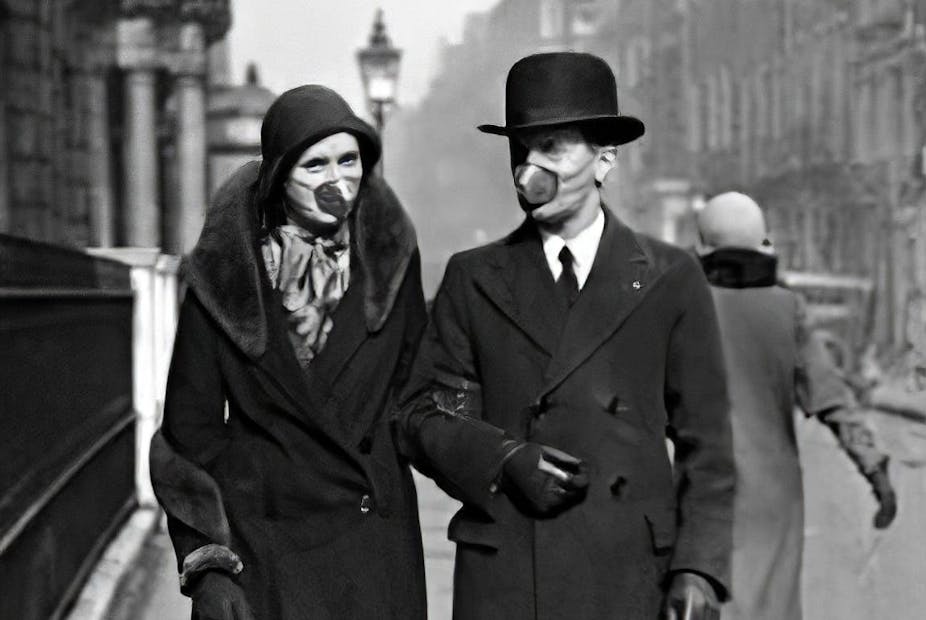 A couple walk down a street in 1918 wearing masks.