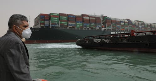 A man in a mask on a boat in fron tof the Ever Given container ship