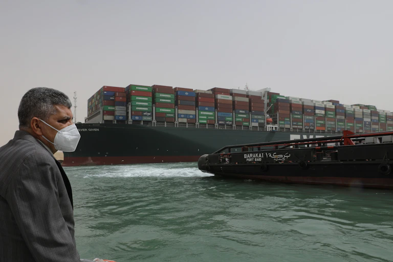 A man in a mask on a boat in fron tof the Ever Given container ship