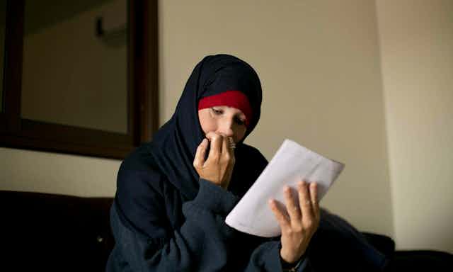 Woman wearing a hijab sits reading a letter