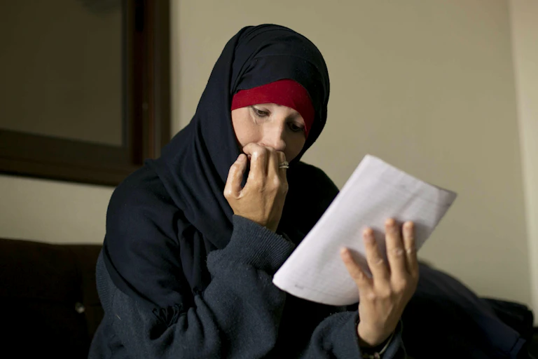 Woman wearing a hijab sits reading a letter