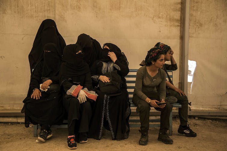 Women wearing niqabs sit huddled together on a bench