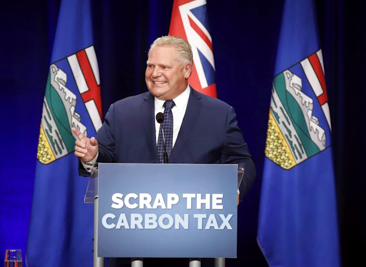 Doug Ford stands behind a podium with a sign reading 'Scrap the carbon tax'