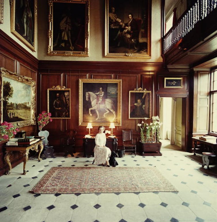 A woman in a grand room, surrounded by paintings.