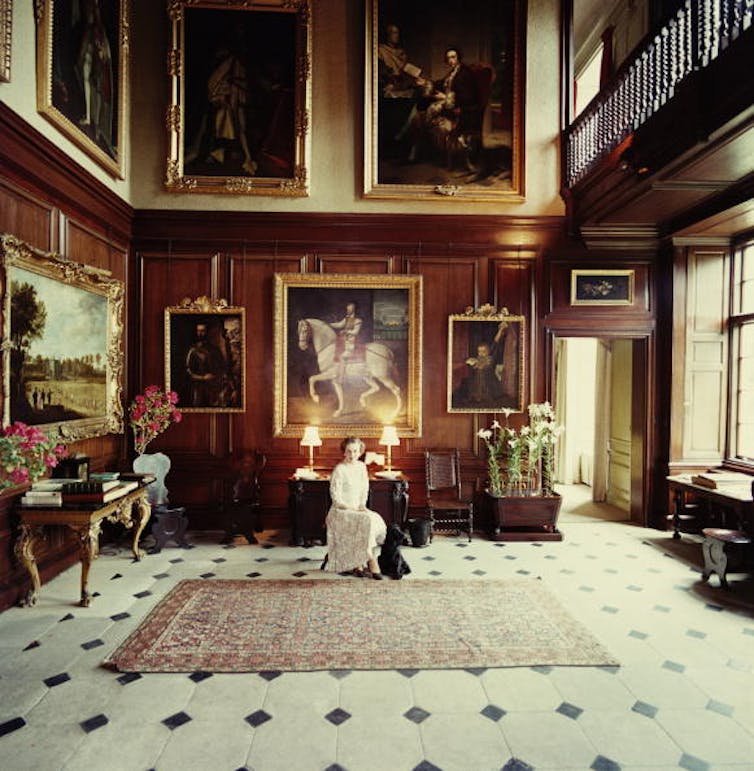 A woman in a grand room, surrounded by paintings.