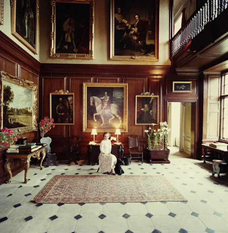 A woman in a grand room, surrounded by paintings.