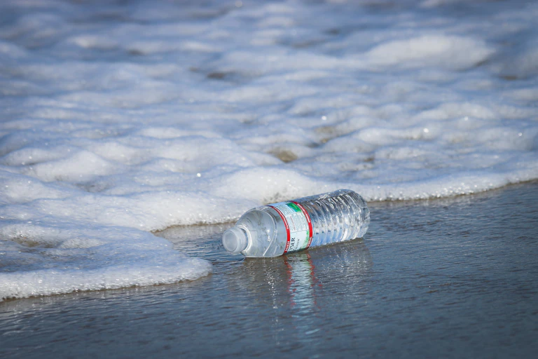 Botol air plastik terkena ombak di pantai.