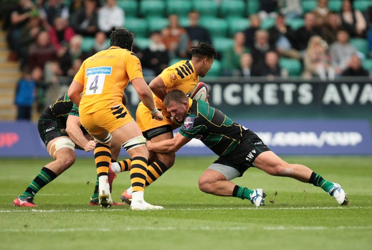 A rugby player is in the middle of tackling another player from the opposing team.