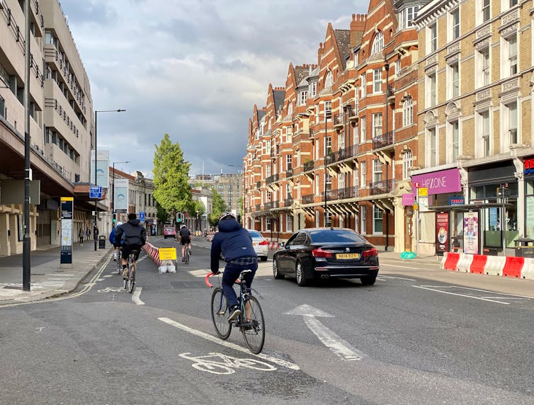 Cycling is 10 times more important than electric cars for reaching net-zero cities. Cyclists pass cars on the left in a temporary cycle lane in Hammersmith, London, UK.