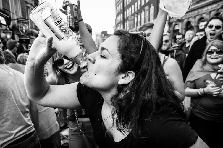 Street party with woman in the foreground drinking from a bottle.