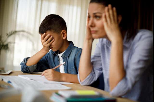 A young boy and his mother sit at a table frustrated while trying to complete their math homework.