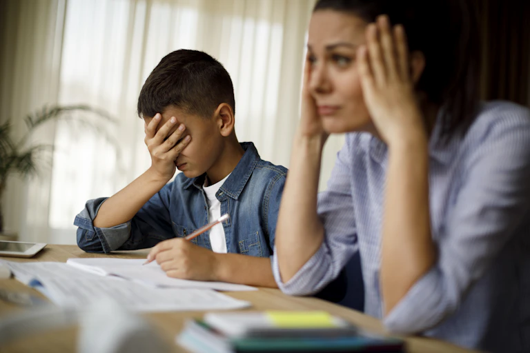 A young boy and his mother sit at a table frustrated while trying to complete their math homework.