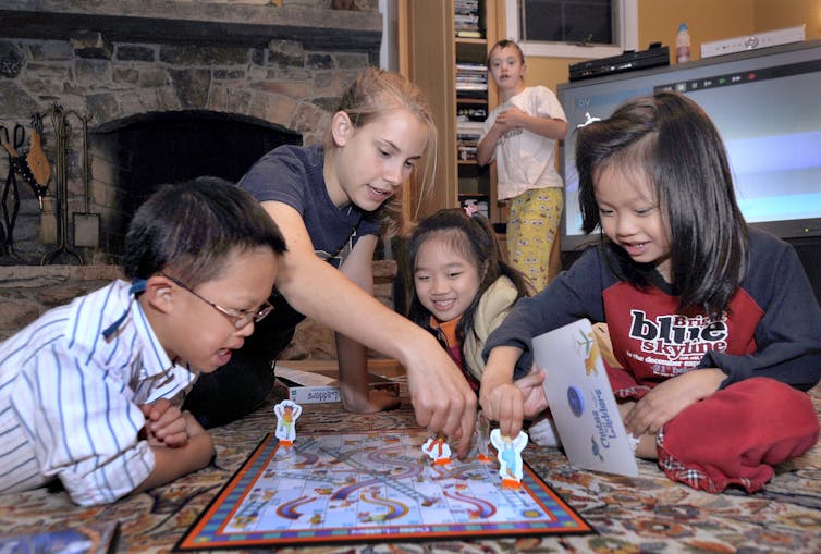 A group of children gather to play Chutes and Ladders on the floor.