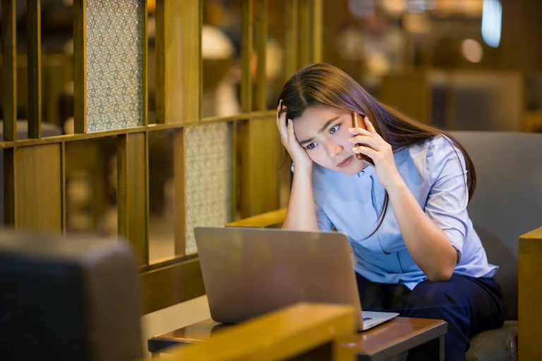 Woman sits looking at computer on phone, worried