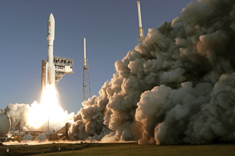 A rocket ship lifts off with clouds of smoke in the foreground.