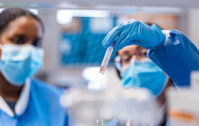 two masked women look at the test tube one is holding up