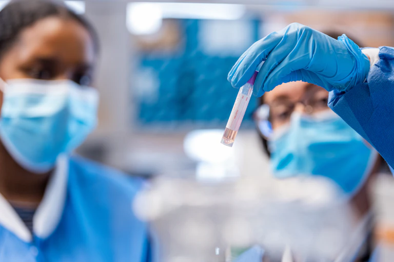 two masked women look at the test tube one is holding up