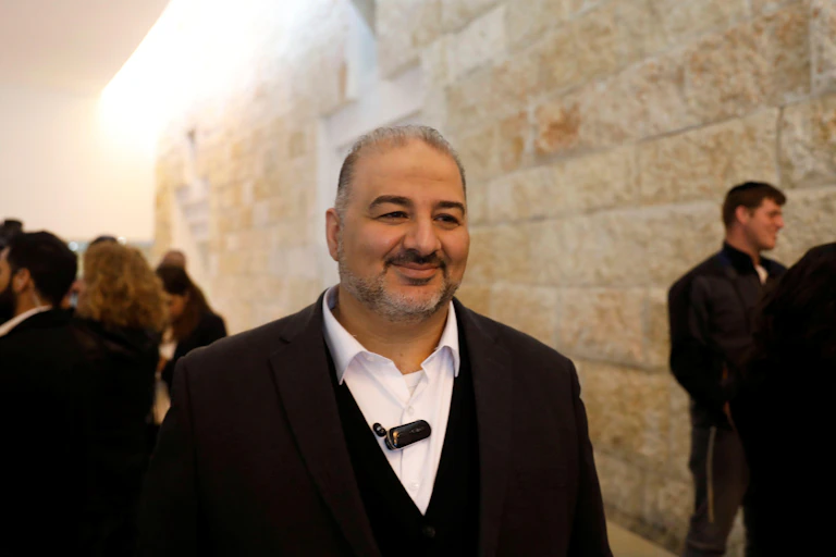 Smiling middle-aged man in a suit and open-collared shirt walking along a street in Jerusalam, March 2019.
