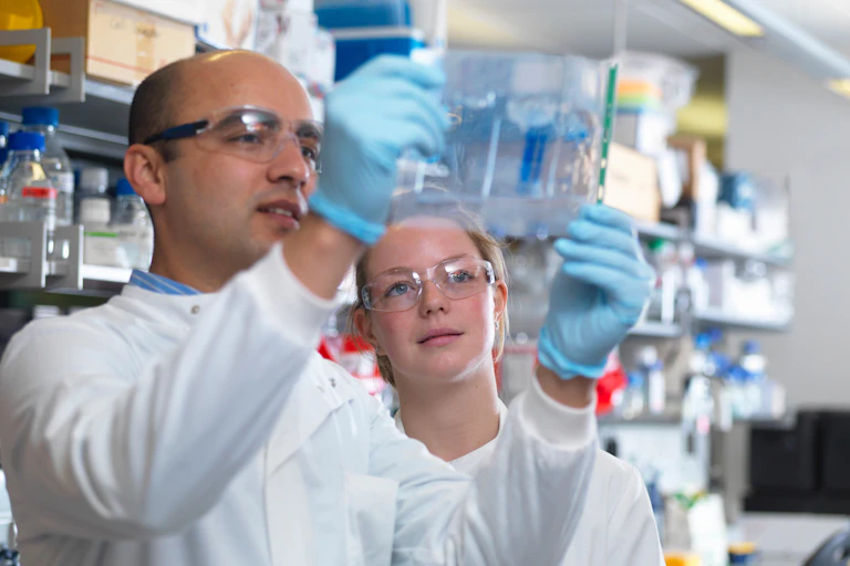 Two scientists wearing white coats and gloves hold up sample in a lab.