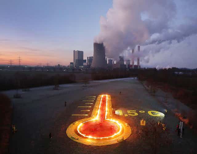 A burning thermometer points to a coal-fired power station in the distance.