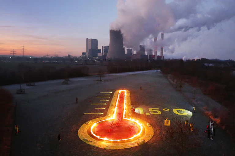 A burning thermometer points to a coal-fired power station in the distance.