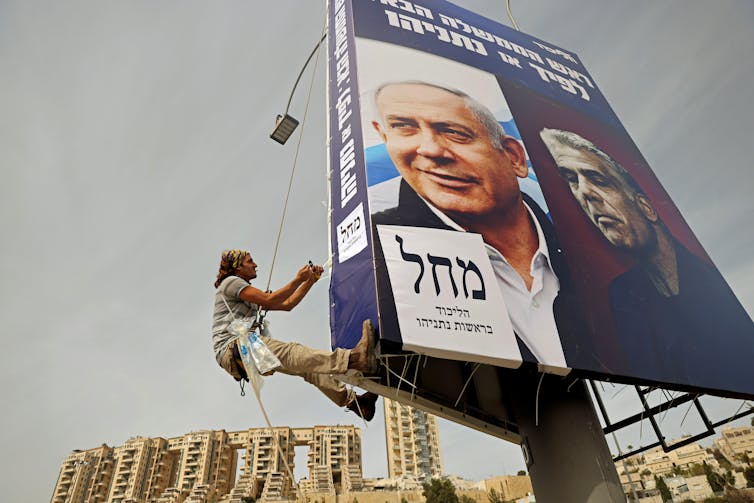 A young man hangs a Likud party election campaign banner, depicting Israeli prime minister Benjamin Netanyahu and his challenger, Yesh Atid party leader, Yair Lapid.