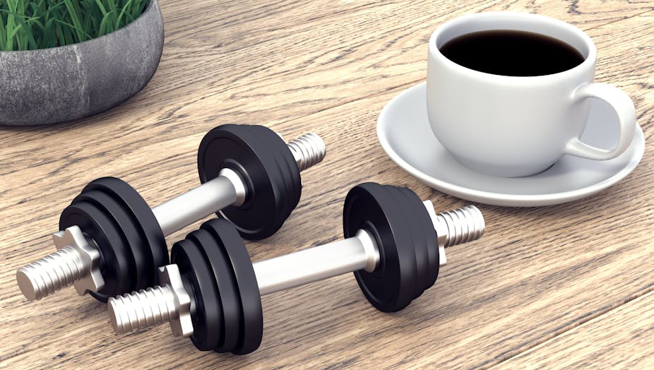 A cup of coffee sitting on a table next to two dumbbells.