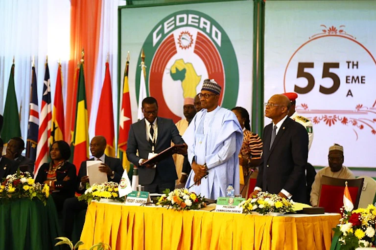 People sitting and standing at a table with flags behind them.