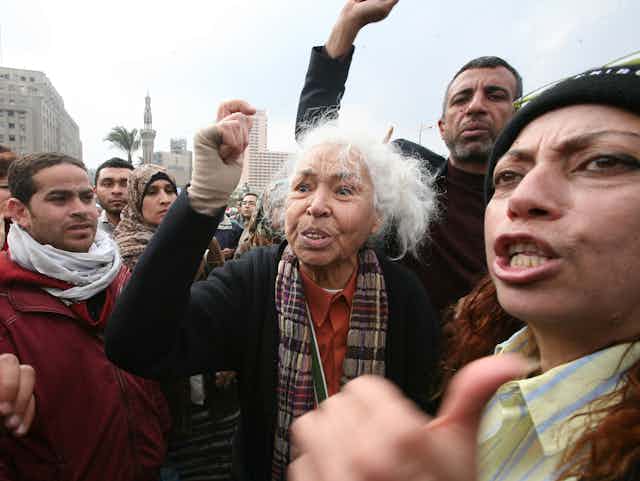 a group of protesters, at their centre a grey-haired woman with her fist raised.