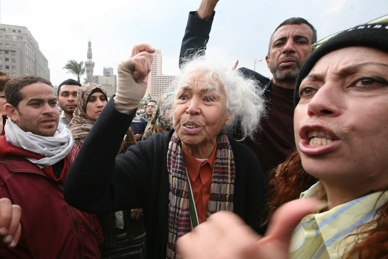 a group of protesters, at their centre a grey-haired woman with her fist raised.