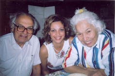Three people smile for the camera, from left an elderly man in thick-rimmed glasses, in the centre a young woman looking glamorous and on the right a grey-hairs woman in a striped blouse.