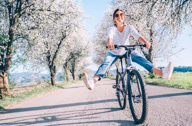 Happy smiling woman on bicycle on the country road under blossom trees. 