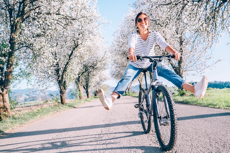 Happy smiling woman on bicycle on the country road under blossom trees.