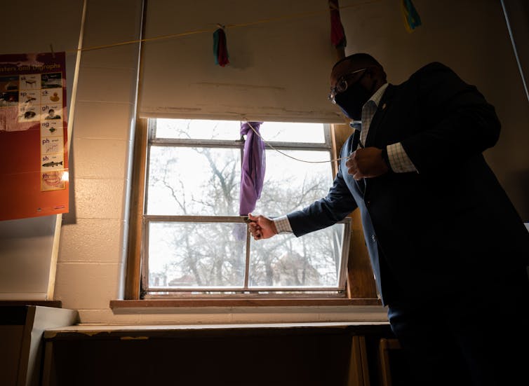 Man in suit opens window of school classroom