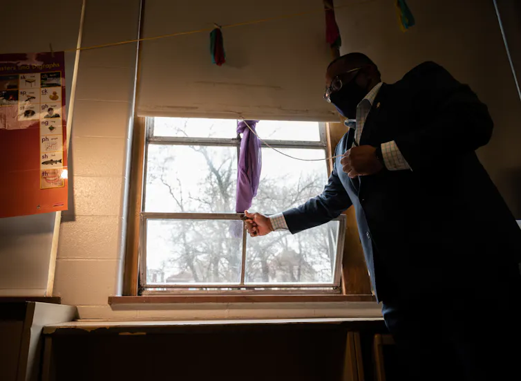 Man in suit opens window of school classroom