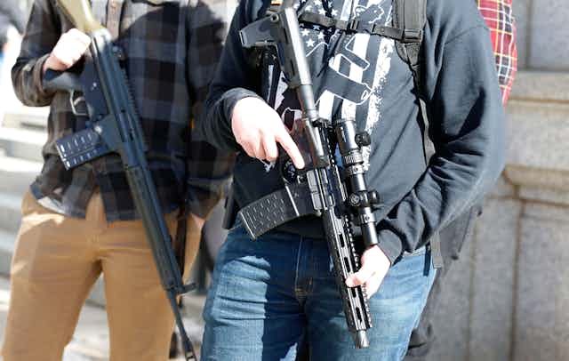 Two people carrying assault-rifle style firearms