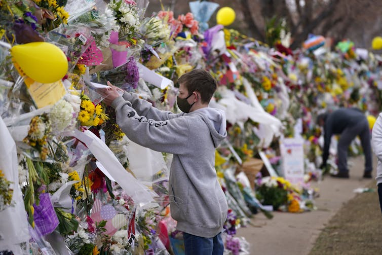 A person places an item in a wall of flowers and messages mourning the victims of the Boulder supermarket shooting.
