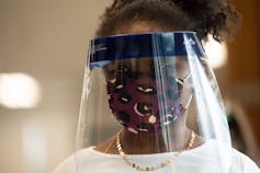 A young black girl wears a mask and a face shield over her face.