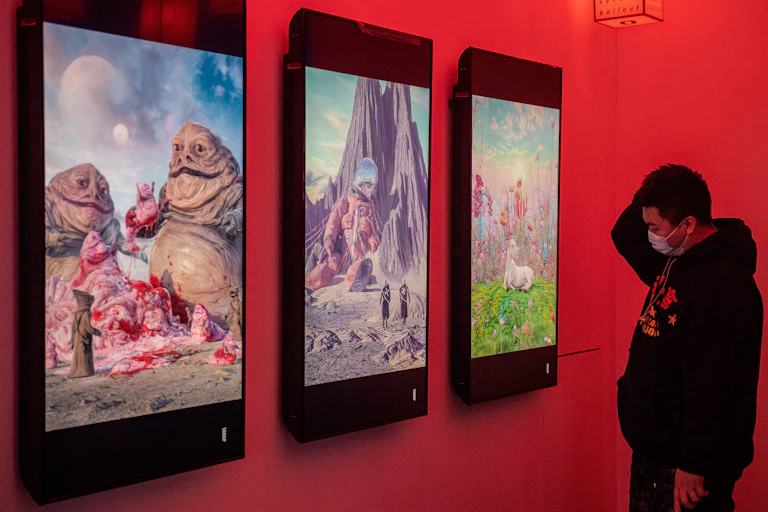 A man wearing a facemask looks at digital paintings by US artist Beeple