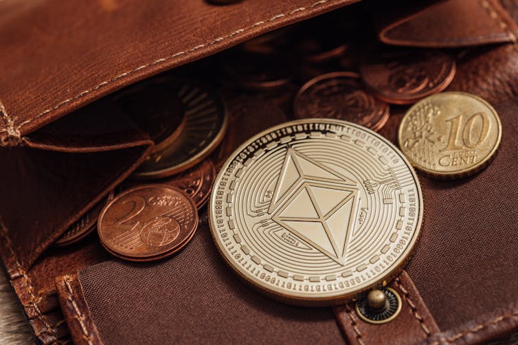 A commemorative coin bearing a double-pyramid logo lies in an open leather wallet containing euro coins
