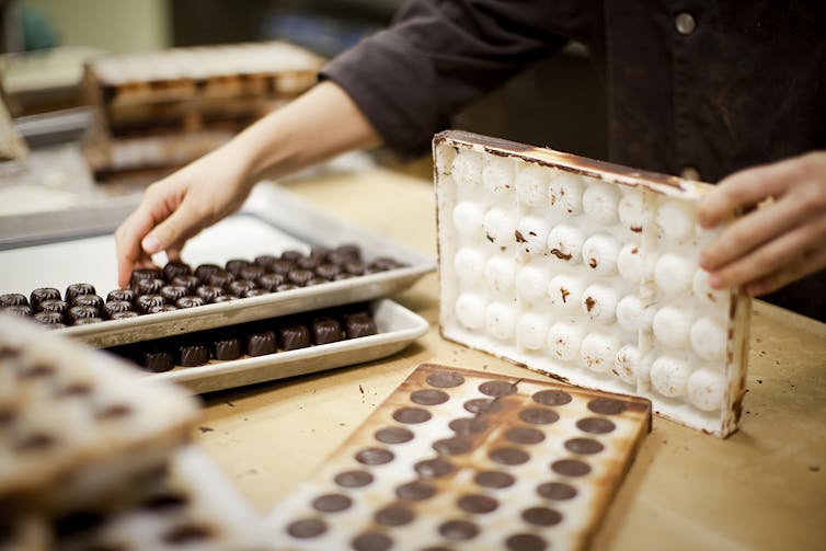 as mãos de um fabricante de chocolate removem os doces acabados de uma forma de chocolate