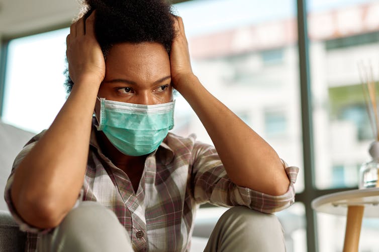 A man wearing a surgical mask with his hands on either side of his head.