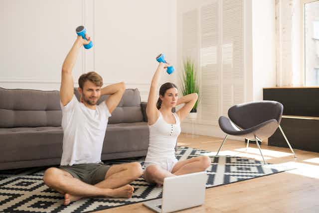 Man and woman sit doing at home workout