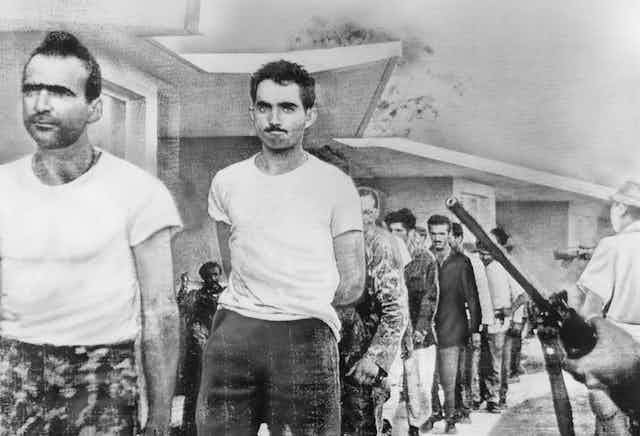 Grim-faced men march under the eye of armed Cuban guards.