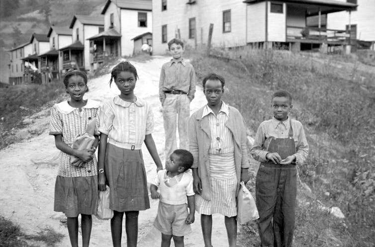 Five Black children stand in the foreground while a white boy stands in the background.