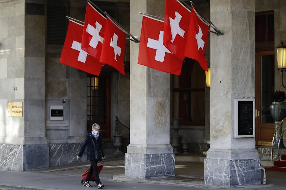 A woman walks past the Swiss flags wearing a protective mask