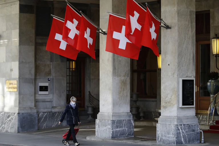 A woman walks past the Swiss flags wearing a protective mask