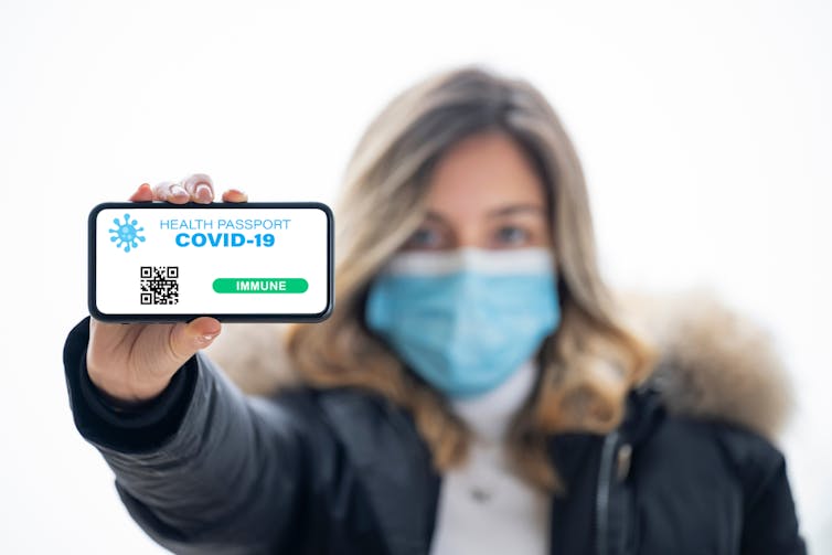 Woman with mask holding up vaccine passport on phone