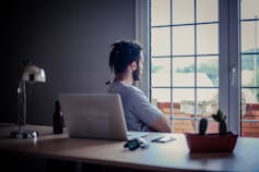 Man with his back to his desk, looking out a window.